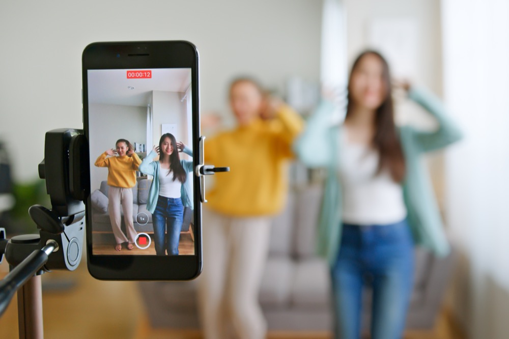 a teenage Asian woman with her tiktoker friend created her dancing tiktok video by smartphone camera together to share on social media