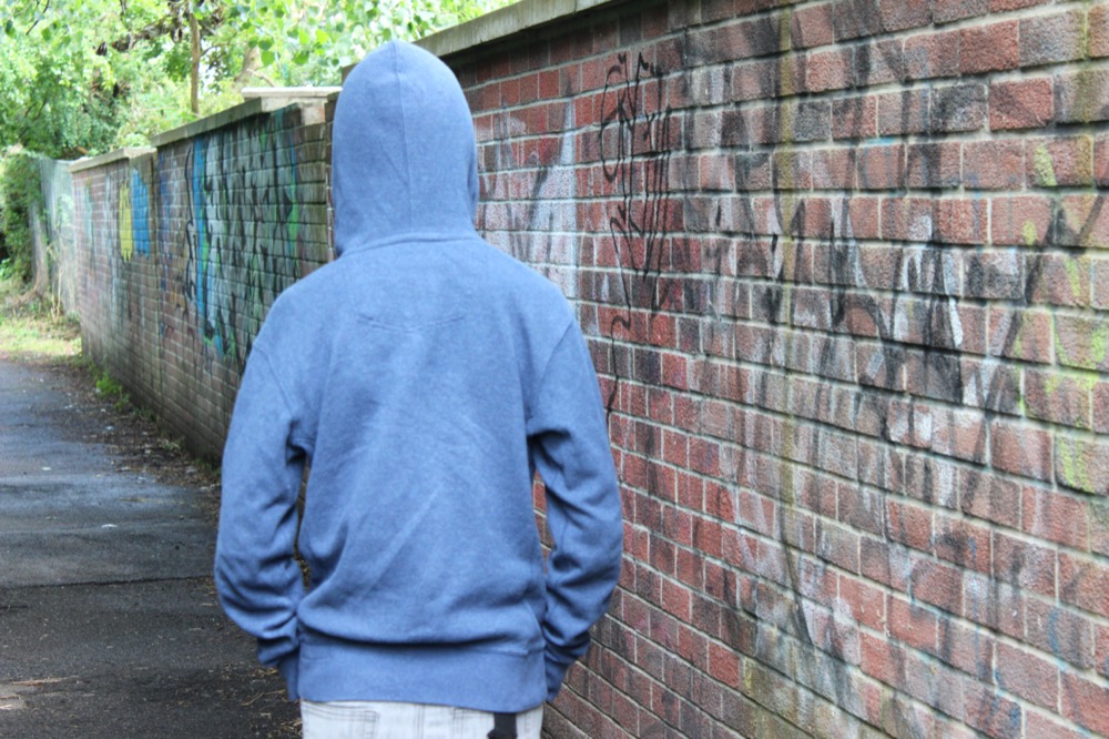 Image of teenage boy youth wearing hoodie, walking beside graffiti wall