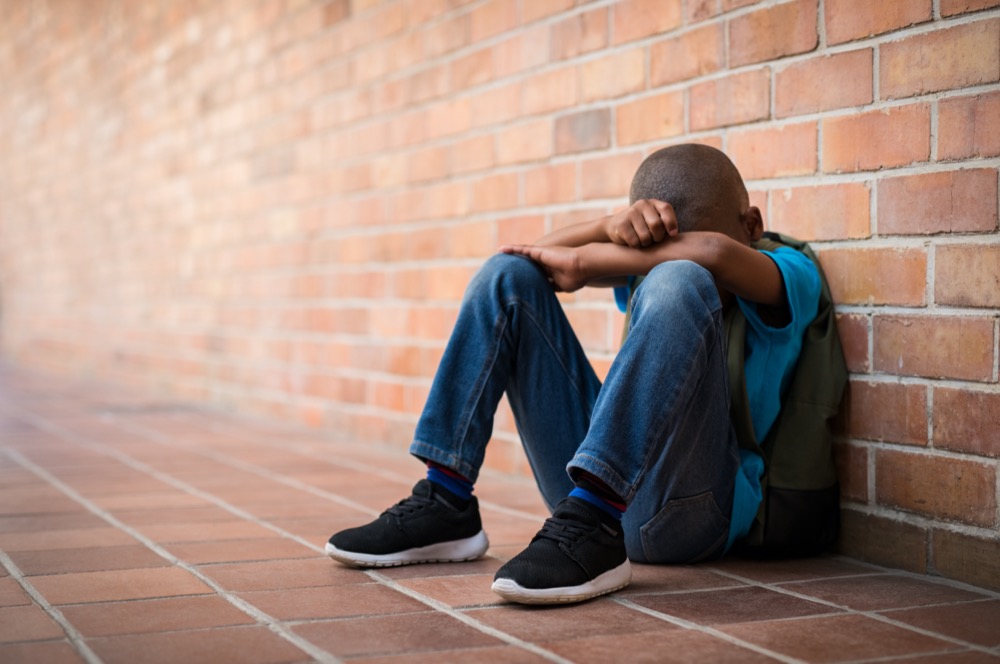 teenage boy having a mental health crisis is crying against a brick wall